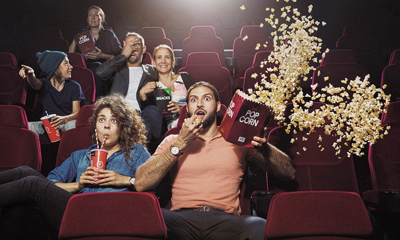 En biosalong men flera personer som ser rädda och chockade ut och kastar ut popcorn i luften