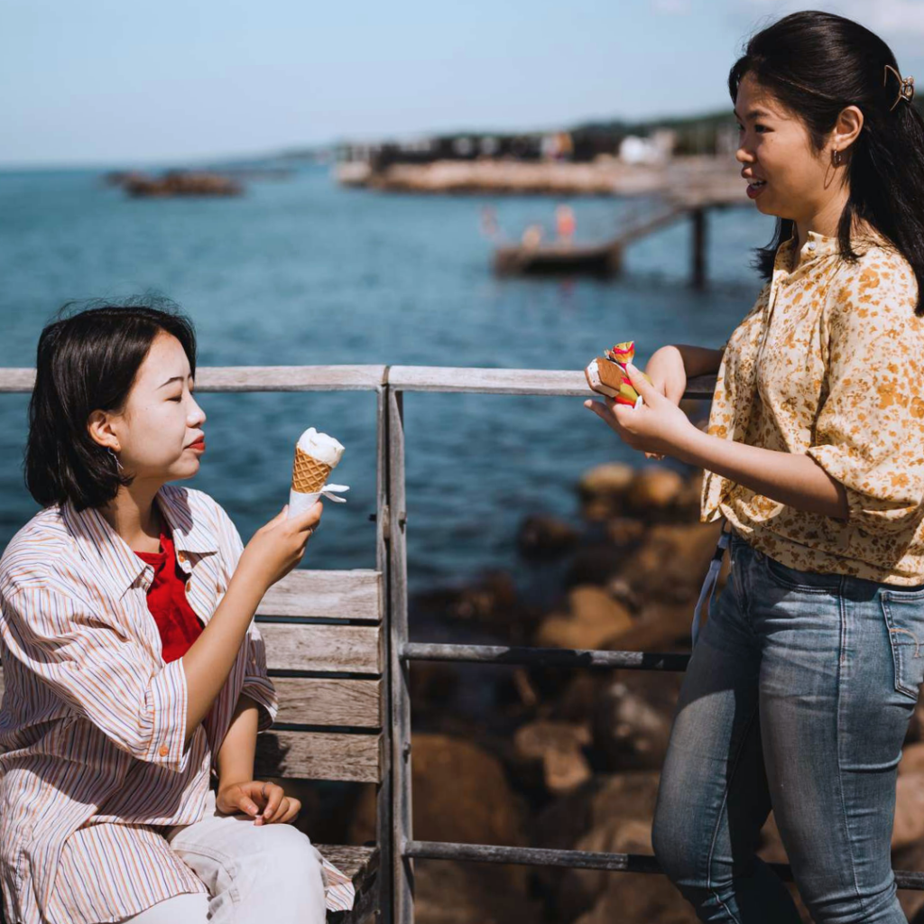 Två tjejer äter glass vid havet