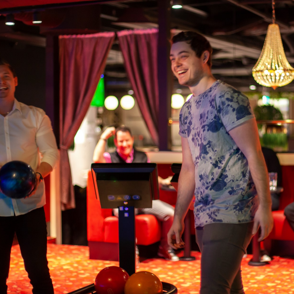 två personer på bilden, de står i en bowlinghall, de ler och är på väg att kasta sina klot