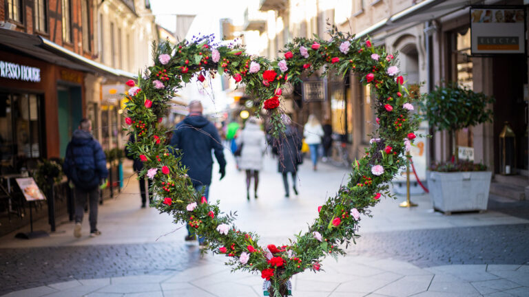 ett hjärta gjort av blommor och växter som står på en gata, vi ser personer i bakgrunden