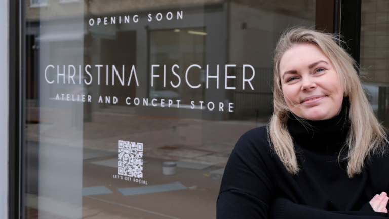 En kvinna står framför ett skyltfönster där det står Christina Fischer och opening soon.