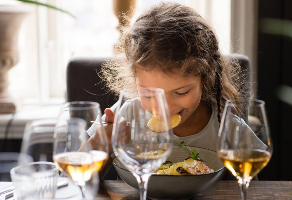 Ett barn äter på middag på restaurang, hen böjer sig fram för att ta en tugga.
