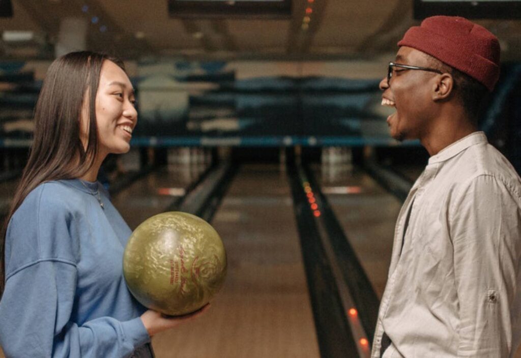 Två ungdomar står framför varandra i en bowlinghall, den ena håller ett klot och de båda ler.