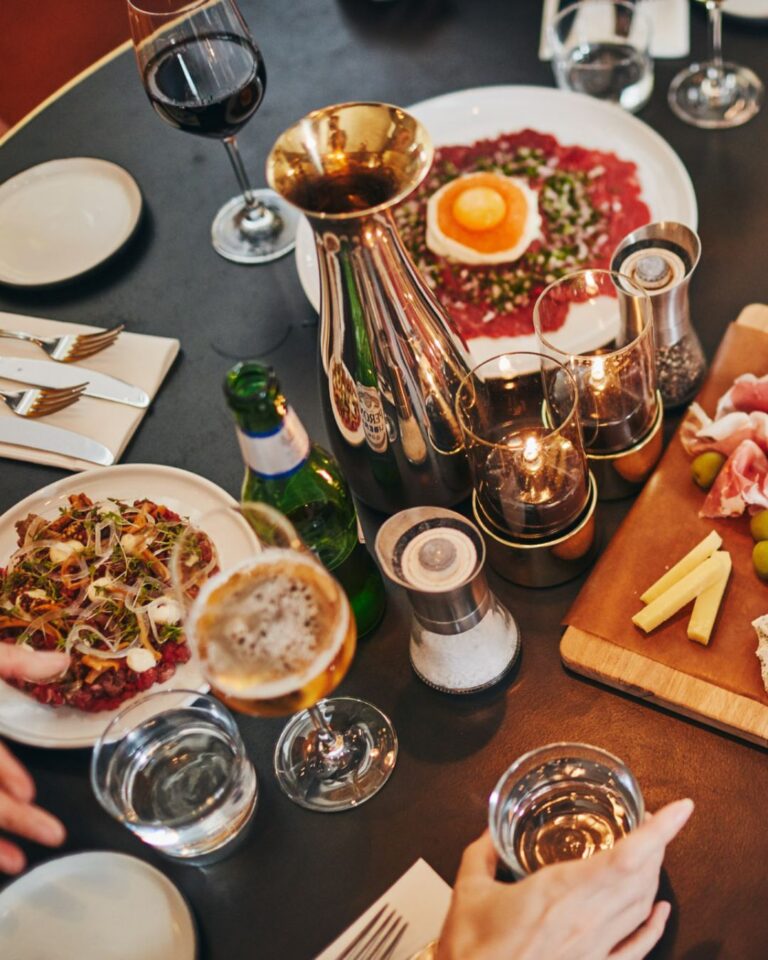 Ett bord fyllt med tallrikar med olika maträtter och glas som är fyllda med dryck, ljus på bordet och man ser några händer