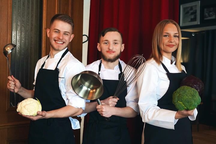Student takeover på The Social Restaurang i Helsingborg. På bilden ser man tre personer som har svarta förkläde och vita skjortor på sig och håller i olika köksredskap.