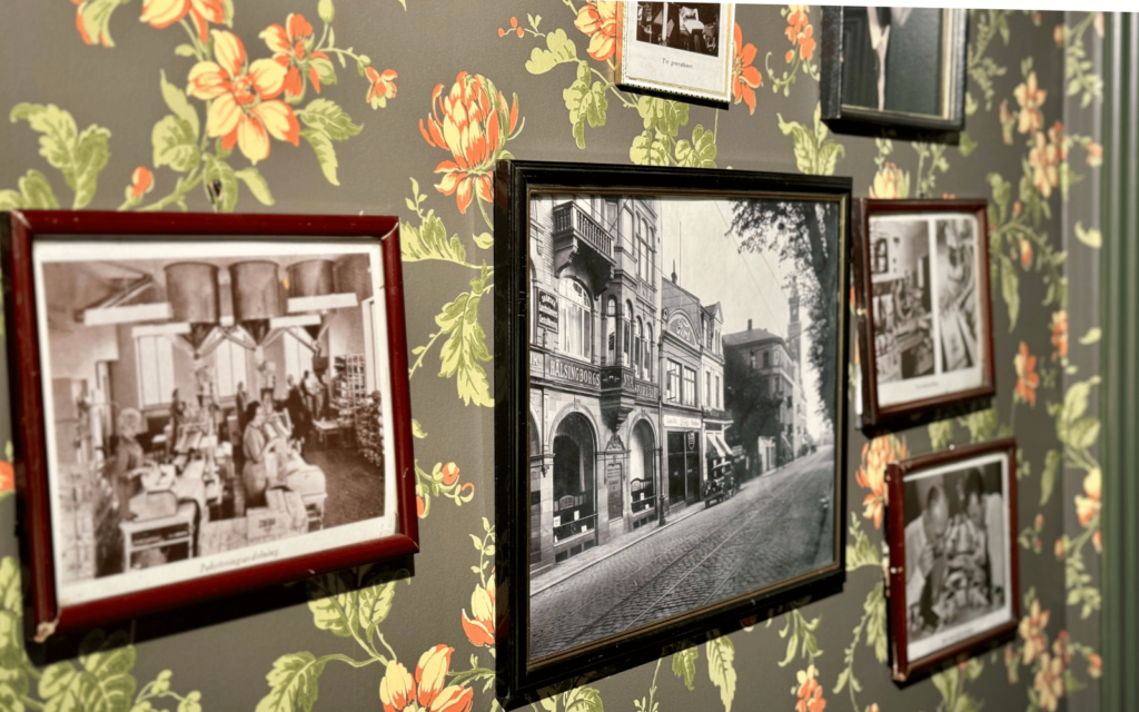 På en vägg med blommig tapet hänger flera tavlor med svartvita fotografier som föreställer Helsingborg på mitten av 30-talet.