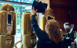 En kvinna håller kaffebönor från en stor hink i en gammeldags kaffekvarn.