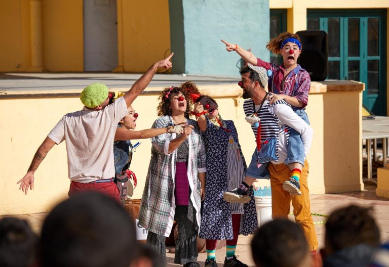 Clowner som står på en scen och pekar och skrattar i olika färgglada kläder.