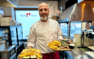 En man står med två tallrikar i handen, en med kebab och en med fajita.