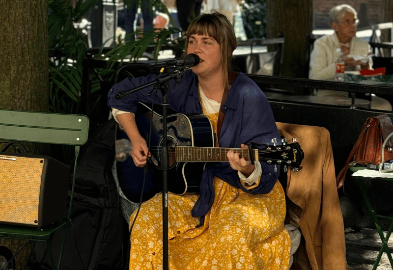 En kvinna sitter på en stol och spelar gitarr och sjunger i en mikrofon.