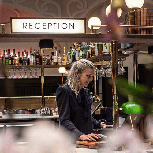 En kvinna står i receptionen på ett hotell redo att checka in gäster som ska bo där över natten