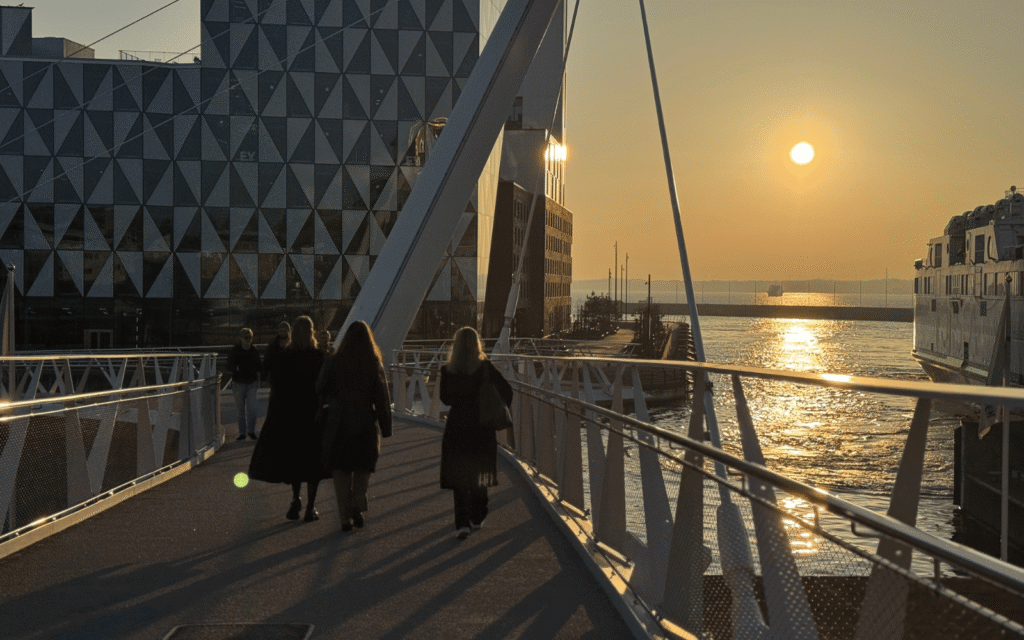 Tre personer som går på en bro med solnedgången som lyser över Öresund