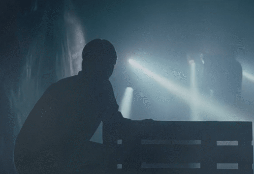 Ett mörkt rum, ser en gestalt som gömmer sig och i bakgrunden är et personer med ficklampa