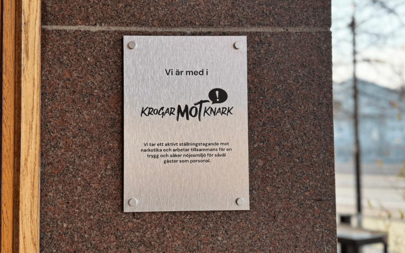 En silvrig skylt uppsatt på en stenvägg med texten Krogar mot Knark.
