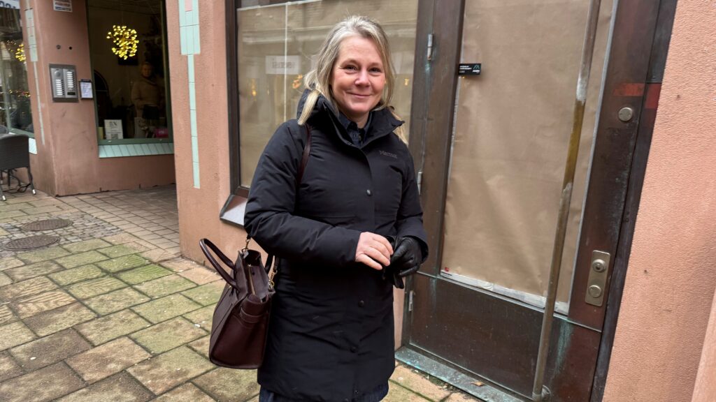 En kvinna i start jacka och brun handväska står framför ett skyltfönster som har brun pappa för fönsterna.