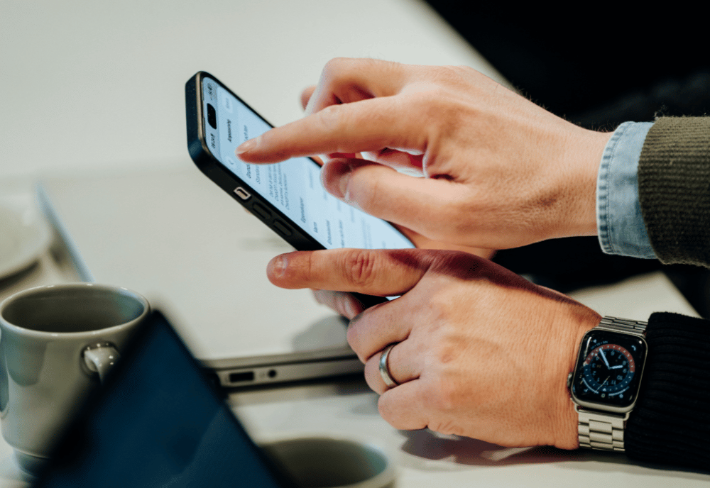 En hand håller i en mobiltelefon och en annan hand pekar på skärmen.