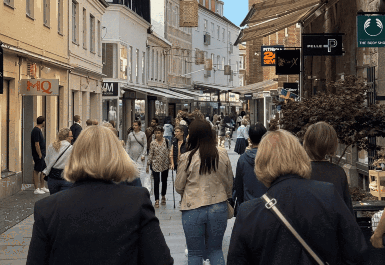 En gågata med butiker och verksamheterna längst sidorna och flera människor som går på gatan.