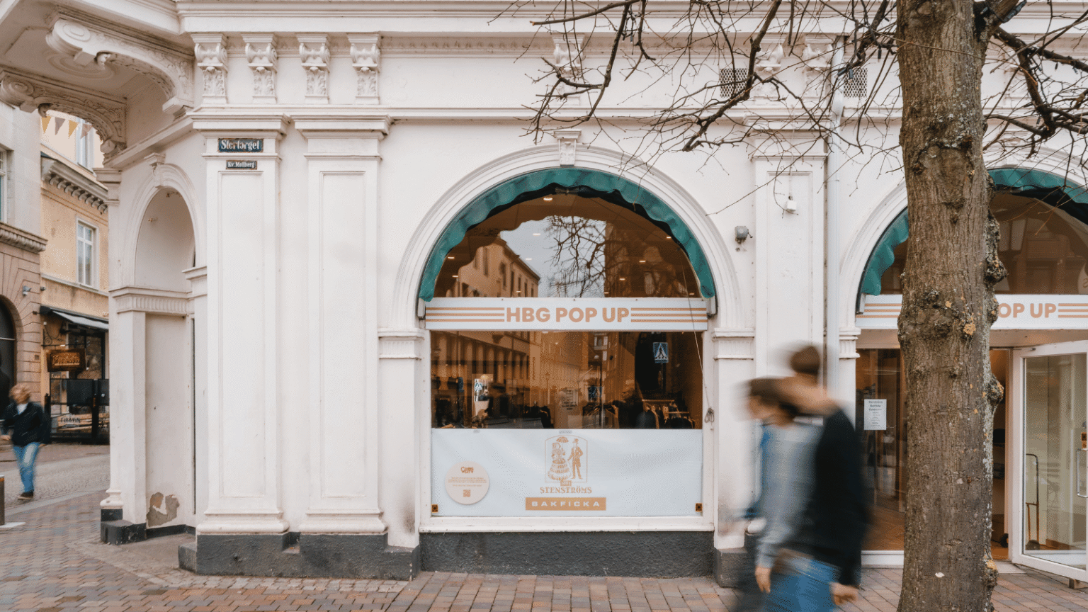 En vit fastad på en byggnad i sekelskiftsstil. På skyltfönsterna till butiken står det HBG POP UP med orangea bokstäver.