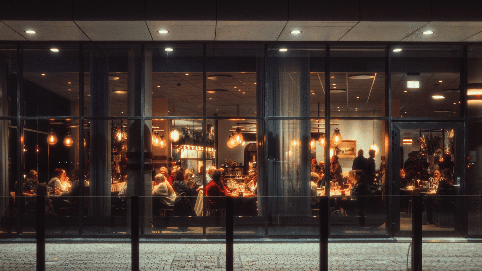 En bild på en restaurang tagen utifrån så att man ser in genom fönstret.