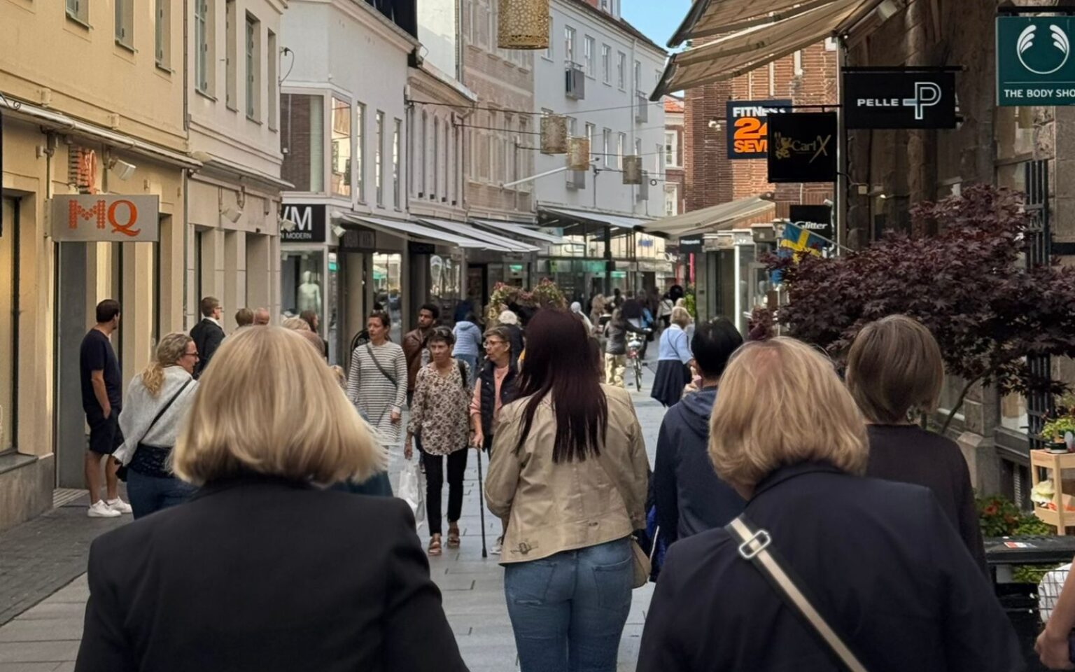 En gågata med butiker och verksamheterna längst sidorna och flera människor som går på gatan.