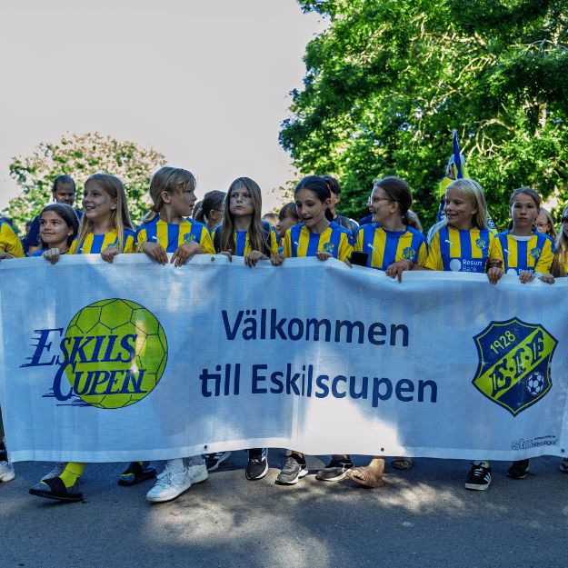 Ungdomar som går utomhus i en parad och håller i en banner där det står Välkommen till Eskilscupen