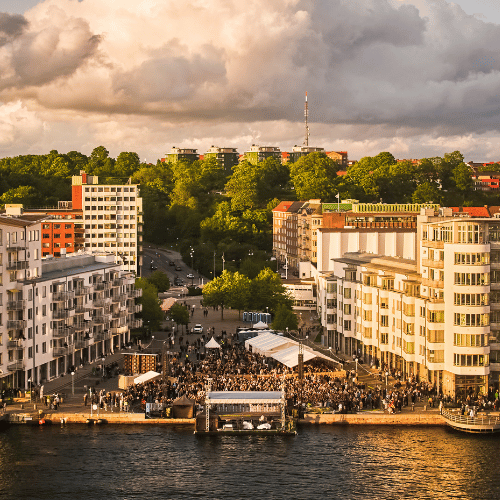 Ett hamnområde med ett stort publikfav mellan höga byggnader precis vid en kajkant.