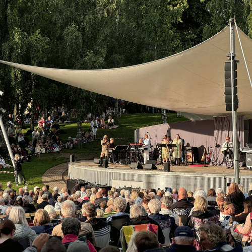 En utomhusscen men artister på scen och en publik som sitter på gräset