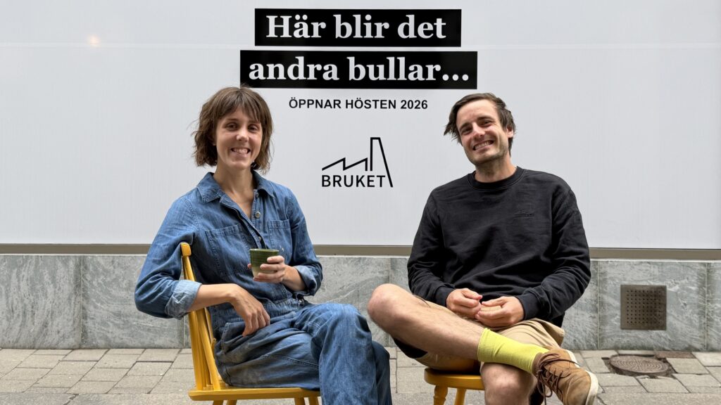 En kvinna och en man sitter på två gula stolar framför ett skyltfönster.