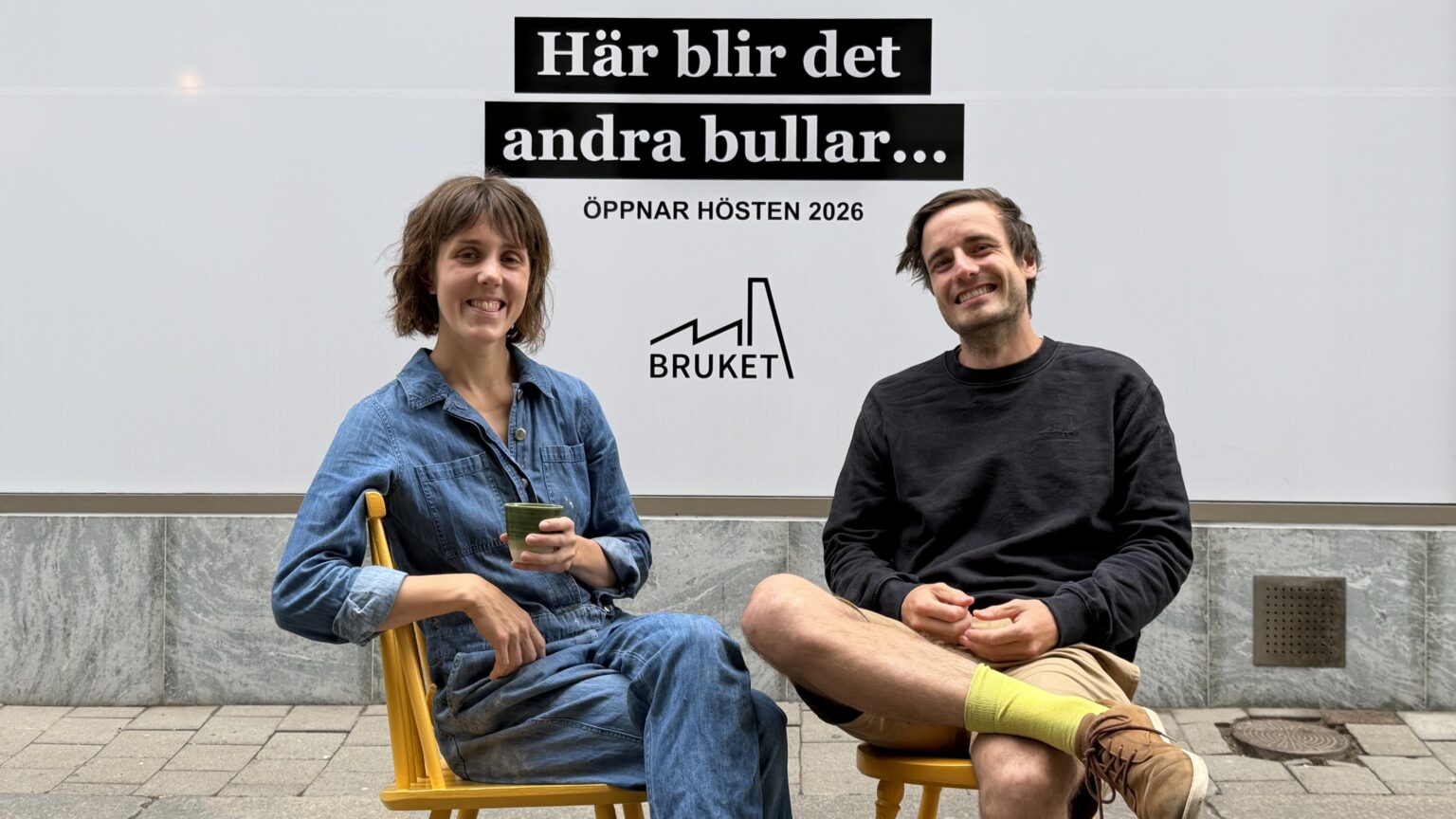 En kvinna och en man sitter på två gula stolar framför ett skyltfönster.