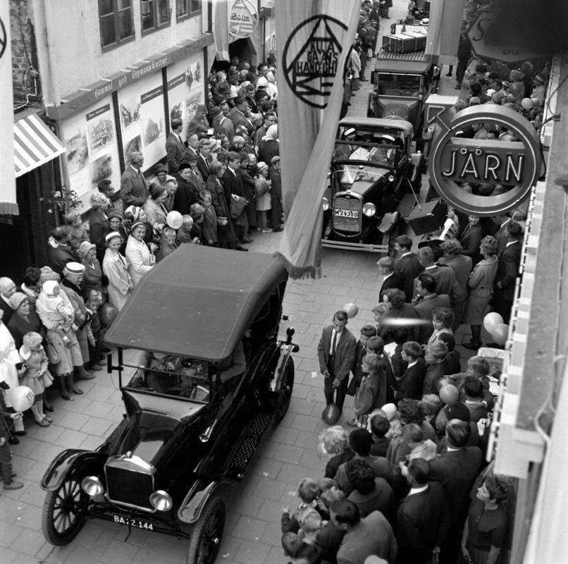 En svartvit bild från invigningen av Kullagatan 1961. Veteranbilar kör längst med gatan och folk står vid sidorna av gatan.