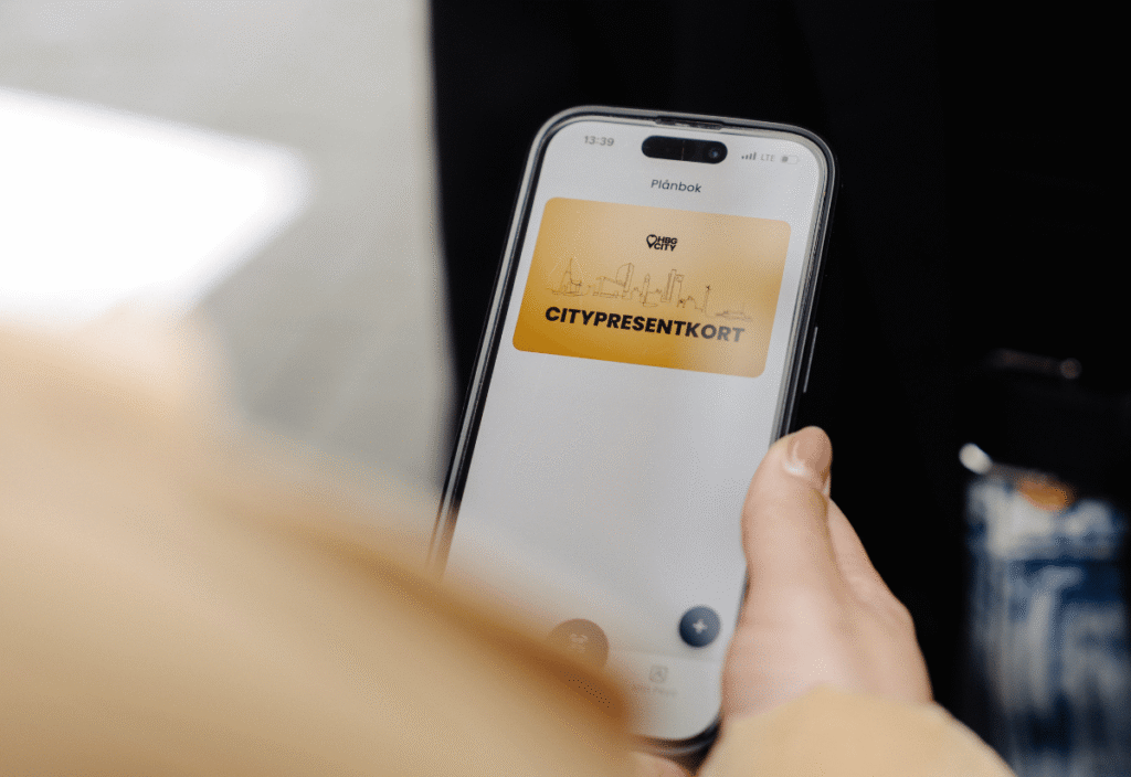 En hand håller i en mobil. På skärmen syns ett guldigt kort med texten Citypresentkort.
