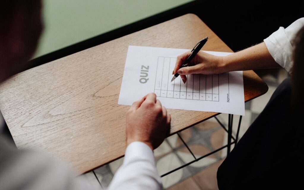 Ett papper ligger på bordet, står quiz och man ser två händer som pekar och skriver