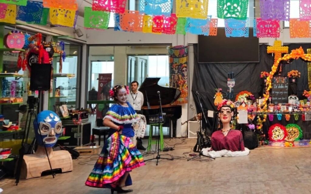 En flicka i färgglada kläder och ansiktsmålning dansar i en sal med dekor från Dia de Muertos.